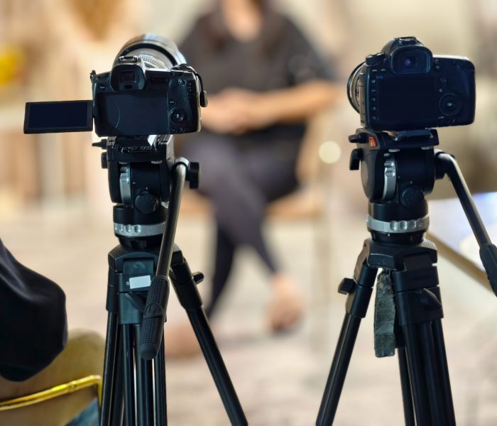 Two cameras are set up on tripods, ready to record a person in the background for a video project